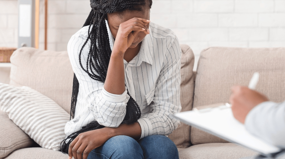 Black woman on couch looking upset, speaking with mental healthcare professional